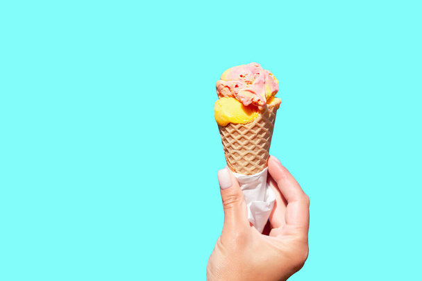 青い背景に対して手のアイスクリームコーン. アイスクリームコーンを持っている女性の手. バニラアイスクリーム - 写真・画像