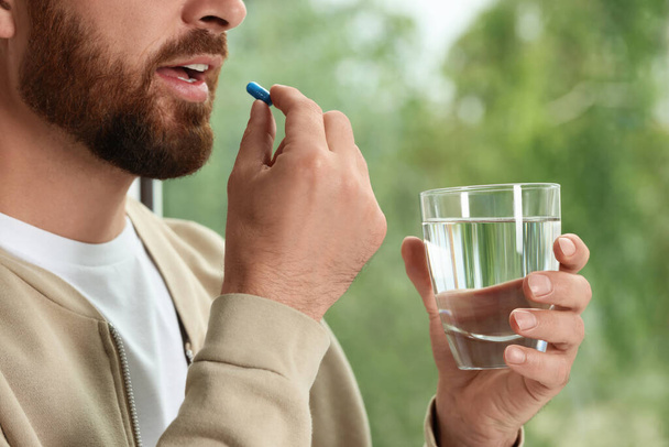 Homem com vidro de água tomando pílula no fundo borrado, close-up - Foto, Imagem