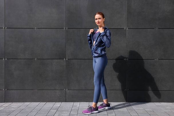 Beautiful woman in stylish gym clothes near dark grey wall on street, space for text - Fotoğraf, Görsel