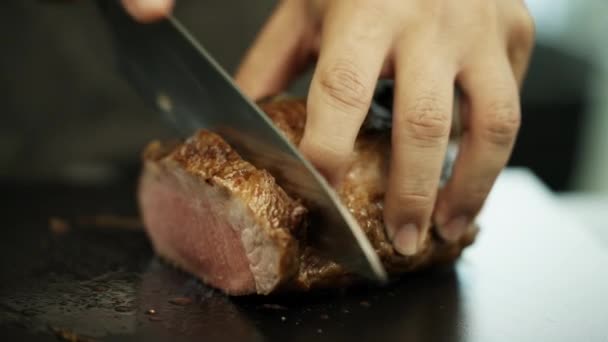 Großaufnahme von fachmännisch geschnittenem iberischen Schweinefleisch auf einem schwarzen Schneidebrett, mit saftigen Fleischstücken und tropfendem Fett. - Filmmaterial, Video