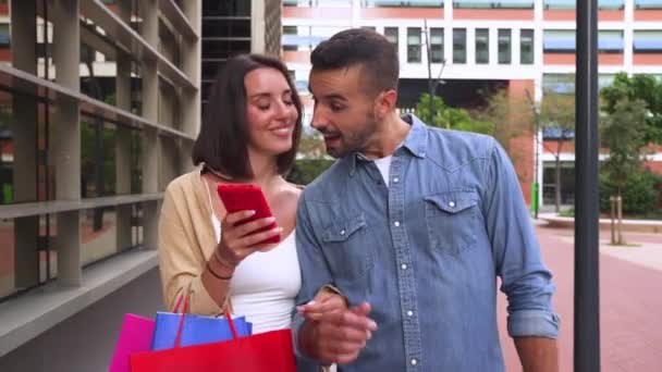 Pretty Kavkazský pár muž a žena držící nákupní tašky, prohlížení aplikací smartphone nákup on-line - Záběry, video