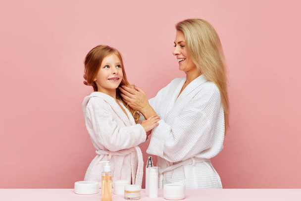 Portrait der schönen Mutter mit Tochter Haarpflege im Badezimmer. Frau und Kind kümmern sich gemeinsam um Schönheit, Gesundheit. Kosmetik und Wohlbefinden der Haut. Konzept der Schönheit, Wellness-Behandlung, Selbstpflege. Anzeige - Foto, Bild