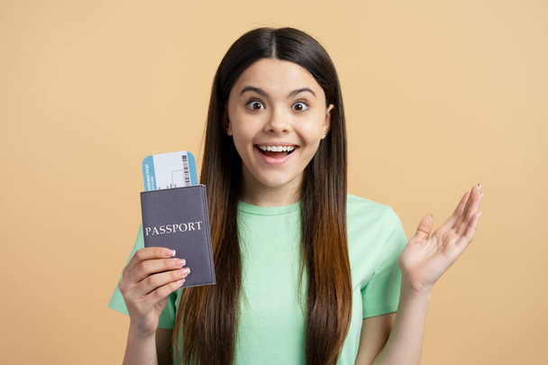 Ritratto di adolescente felice eccitata in possesso di passaporto e carta d'imbarco guardando la fotocamera isolata su sfondo beige. Vacanza, concetto di viaggio - Foto, immagini