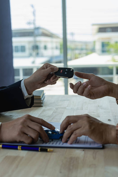 Young salesman holding car keys in hands of car rental business customer sell or buy services Asian male sales representative sells important cars to client tenants. - Photo, Image