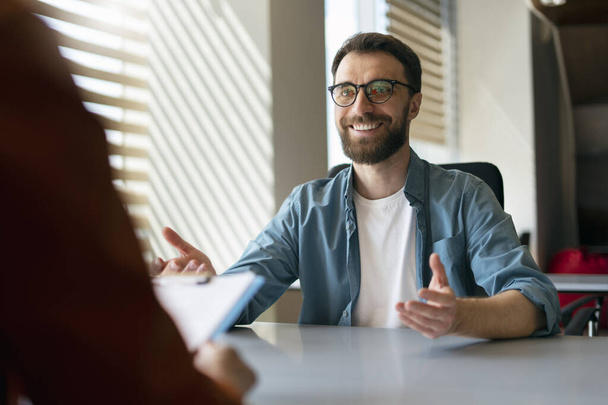 Sebevědomý pohledný usměvavý muž s brýlemi sedící na pohovoru. Podnikatelé mluví, setkávají se, sdílejí nápady v moderní kanceláři. Koncept lidských zdrojů  - Fotografie, Obrázek