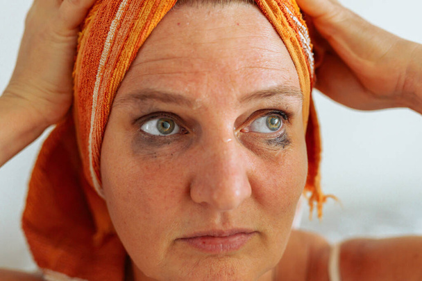 portrait middle-aged woman with towel on wet hair, after shower, with smeared, leaking natural mascara on face. long lasting makeup concept, benefits of cleansing skin from cosmetics, facial skin care - Photo, Image