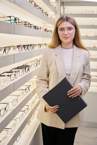 Frau am Arbeitsplatz vor dem Hintergrund eines Schaufensters, im Salon gibt es eine große Auswahl an Brillen - Foto, Bild