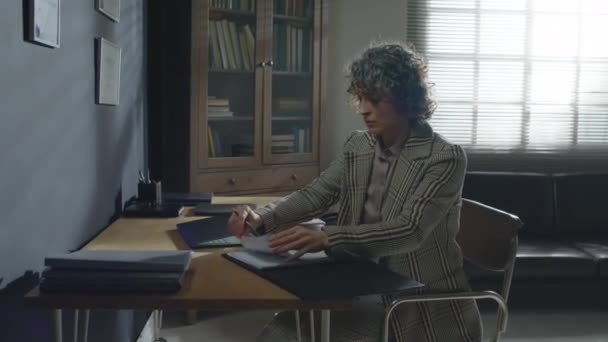 Elegant mature Caucasian female psychotherapist sitting at desk taking sheet of paper and opening laptop - Footage, Video