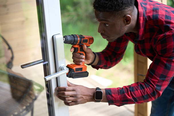 Jovem reparador está reparando uma porta de vidro, ele está usando uma chave de fenda - Foto, Imagem