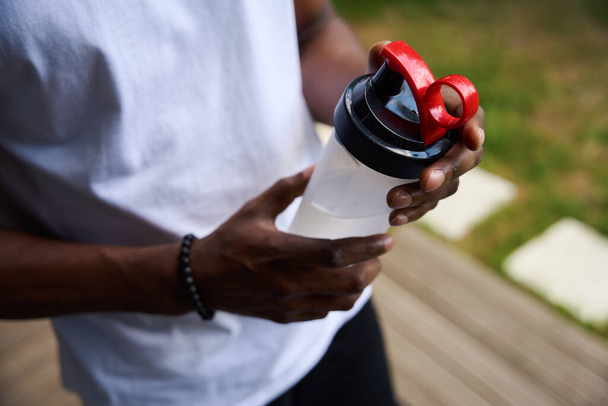 Парень в спортивной форме с чашей с водой, у него браслет на руке. - Фото, изображение