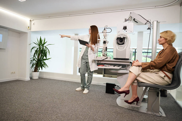 Консультант офтальмолога перевіряє зір пацієнта, жінки знаходяться в яскравому кабінеті - Фото, зображення