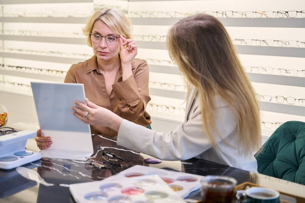 İki bayan optik salonda iletişim kurar, müşteri gözlük seçmede bir danışmandan tavsiye alır. - Fotoğraf, Görsel