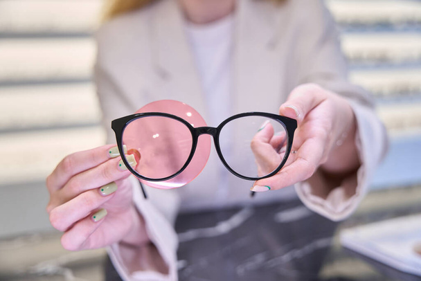 Kobieta trzyma okulary i okulistyczny gadżet w dłoniach, specjalista w jego miejscu pracy w salonie optycznym - Zdjęcie, obraz