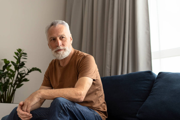 Ritratto di anziano dai capelli grigi solitario che distoglie lo sguardo seduto sul divano in casa di cura  - Foto, immagini