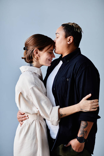 Mutlu eşcinsel çiftin mavi arka planda şefkatle öpüştüğü minimal yan manzara portresi - Fotoğraf, Görsel