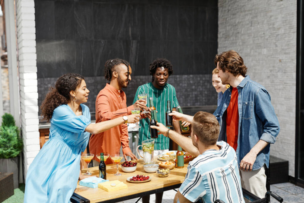 Różnorodna grupa przyjaciół korzystających z kolacji na tarasie w słońcu i brzęczących okularów w święto - Zdjęcie, obraz