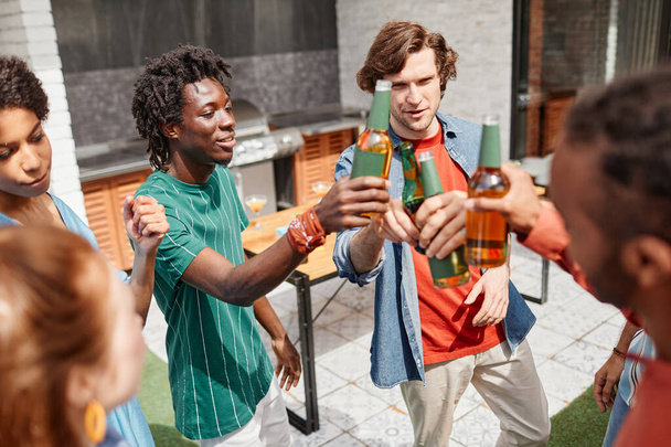 Vista de alto ángulo en un grupo diverso de amigos disfrutando de una fiesta al aire libre y bailando con botellas de cerveza - Foto, Imagen
