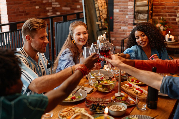 Vielfältige Gruppe junger Leute klirrt bei Dinnerparty in gemütlicher, warmer Atmosphäre - Foto, Bild