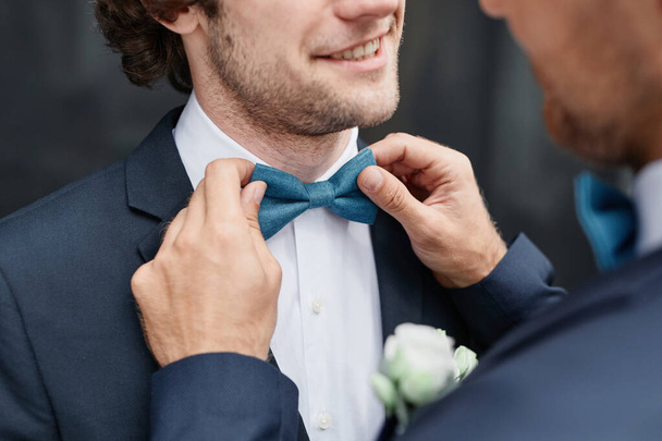 Zbliżenie uśmiechnięty młody człowiek naprawianie muszki pana młodego podczas ceremonii ślubnej, sama koncepcja małżeństwa seksualnego - Zdjęcie, obraz