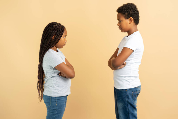 Ritratto di bambini offesi Fratello e sorella afroamericani in piedi e guardarsi con le braccia incrociate isolate su sfondo beige, copiare lo spazio. Concetto familiare - Foto, immagini