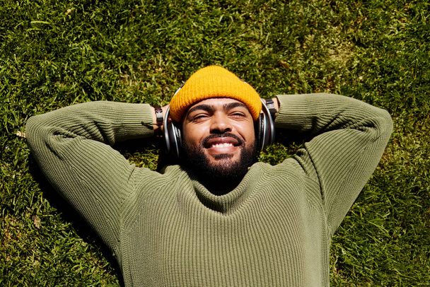Relax, music headphones and happy man on grass outdoor, listen to audio online or hearing sound of podcast from top view. Smile, streaming radio and person at park resting for peace, calm and freedom. - Photo, image