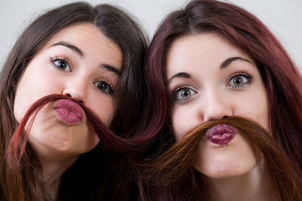 Unbekümmert und strahlend fangen zwei junge Frauen mit makellosem Make-up und Haaren den Geist der Jugend ein, machen urkomische Gesichter und amüsieren sich - Foto, Bild