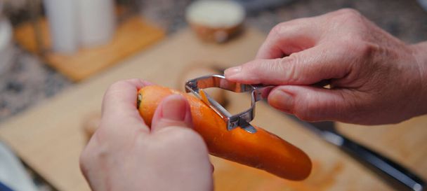 Fechar-se de mãos descascando uma cenoura fresca. Cozinhar alimentos saudáveis. - Foto, Imagem