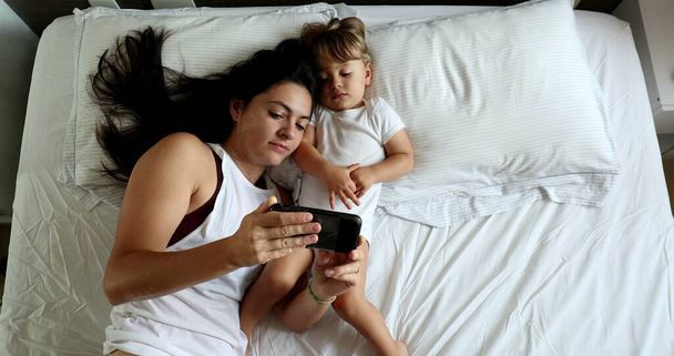 Mother and baby infant watching video on cellphone in bed, top view - Foto, imagen