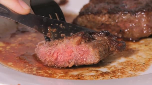 Un gros morceau de steak de bœuf fraîchement grillé dans une assiette. Viande moyennement rôtie avec du sang au ralenti. Un couteau et une fourchette coupent un morceau vue de près - Séquence, vidéo