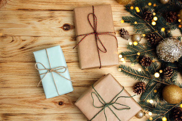 Fondo de Navidad para saludos. Regalos envueltos en papel marrón con ramas de árbol de coníferas, juguetes de Navidad y conos de pino seco sobre un fondo de madera clara. Vista superior - Foto, imagen