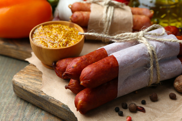 Assortment of thin sausages, mustard in bowl and spices on cutting board, on wooden background - Φωτογραφία, εικόνα