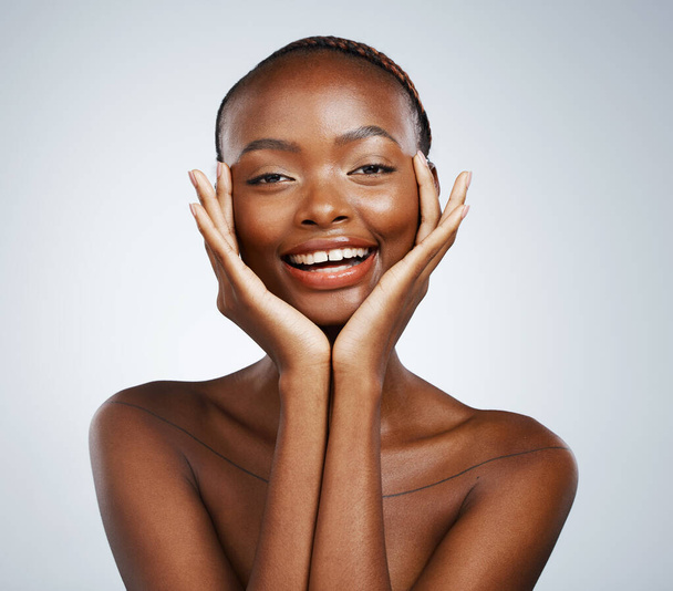 Portret, schoonheid en handen op de wang van een zwarte vrouw in een studio op een grijze achtergrond voor huidverzorging of natuurlijke wellness. Glimlach, spa of luxe en een jong model met cosmetische of anti-aging behandeling. - Foto, afbeelding