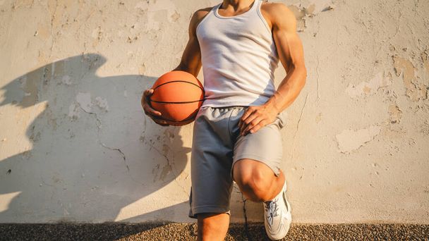 若い白人男性アスリートスタンド屋外ホールドバスケットボールボールウェア白いタンクトップ-シャツ強力な筋肉本人のコピースペース幸せな笑顔自信を持って健康的なライフスタイルのコンセプト - 写真・画像