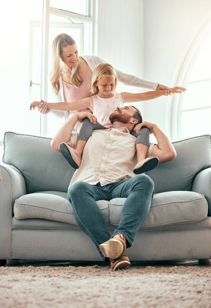 Parents, kid and airplane on sofa, smile and playful for love, care or bonding in living room at family home. Father, mother and daughter with plane game, excited or together on lounge couch in house. - Photo, Image