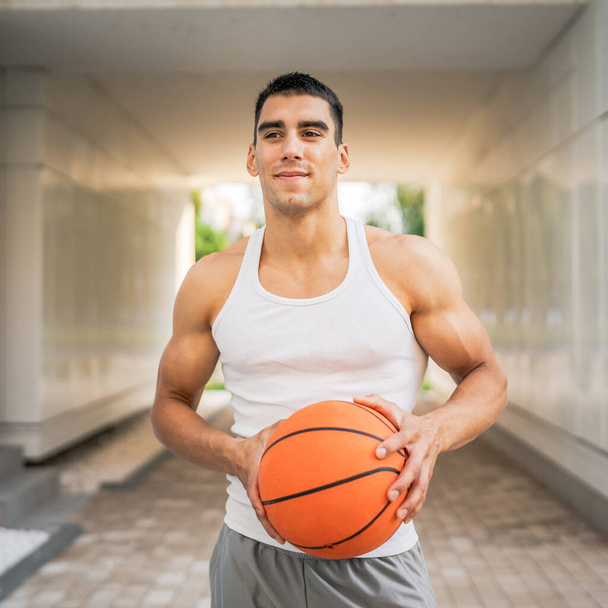 Ein junger kaukasischer Mann männlichen Athleten stehen im Freien halten Basketball-Ball tragen weißen Tank Top a-shirt starke muskulöse reale Person kopieren Raum glücklich Lächeln zuversichtlich gesunden Lebensstil-Konzept - Foto, Bild