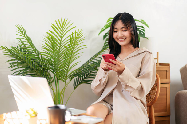 Empreendedora feminina está usando smartphone para verificar as mídias sociais e conversar com amigos enquanto se senta na cadeira para relaxar na sala de estar depois de trabalhar em casa. - Foto, Imagem
