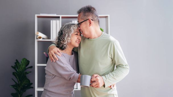 Senior couple kiss and hugging with love while drinking coffee and spending time to doing activity for relaxation in life retirement together at living room of home. - Foto, afbeelding