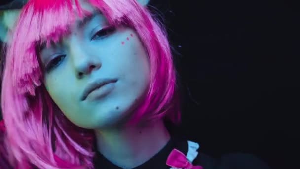 Close-up estúdio retrato de confiante jovem mulher vestindo rosa peruca e gato orelhas cosplay anime personagem de pé contra preto parede posando na câmera - Filmagem, Vídeo