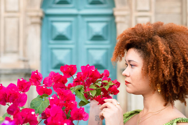 Hermosa mujer pelirroja entre flores lila y roja con hojas verdes. Concepto de amor y cuidado de la naturaleza. - Foto, imagen