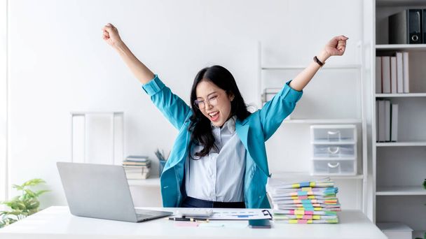 会計業務の概念,会計士の女性は興奮してノートパソコン上で良いニュースを読み取り、ビジネスプランニングファイナンスへの投資に取り組む中で達成を祝うために拳を上げる. - 写真・画像