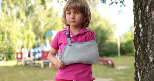 Malý, pohledný chlapec se zlomenou rukou zabalenou v obvazu. Zraněné dítě na hřišti. - Fotografie, Obrázek