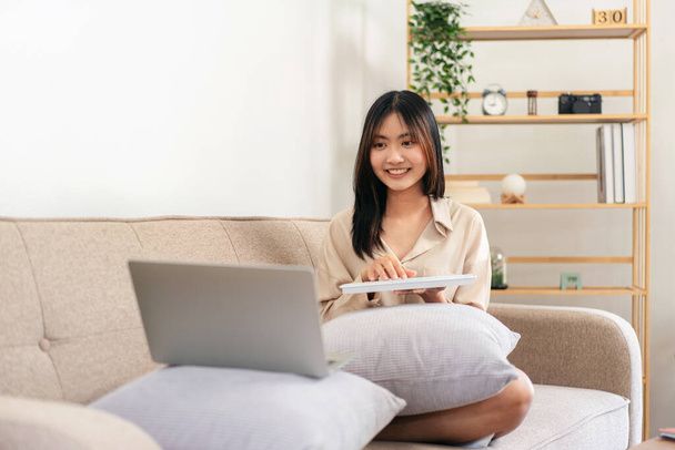 Жінка-підприємець сидить на великому зручному дивані і кладе ноутбук і клавіатуру на подушку для набору бізнес-даних під час роботи у вітальні вдома. - Фото, зображення