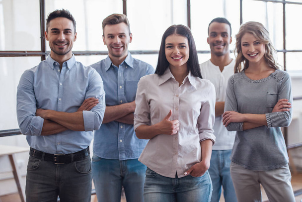 Succesvolle business team is camera kijken en glimlachen terwijl je met gekruiste armen in kantoor - Foto, afbeelding
