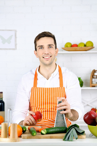 Man at table with different products and utensil in kitchen on white wall background - Φωτογραφία, εικόνα