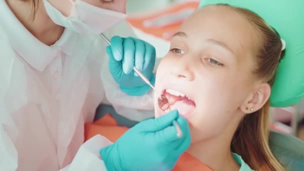 Zubař vyléčení bolesti zubů dospívající dívky, vyšetření zubů s malým zrcadlem a speciálními nástroji, prevence zubních kazu a periodontitidy, každoroční stomatologická prohlídka - Záběry, video