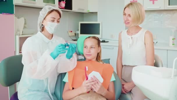 стоматолог женщина объяснение и преподавание пациентка-подросток и ее мать в медицинском кабинете, урок о гигиене зубов, сохранить здоровье и предотвращения кариеса и пародонта - Кадры, видео