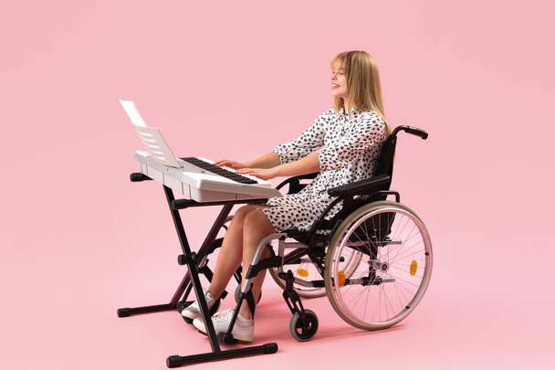 Giovane donna in sedia a rotelle che gioca sintetizzatore su sfondo rosa - Foto, immagini