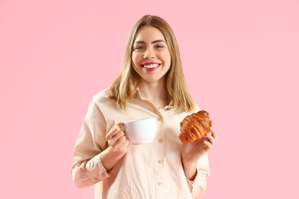 Hermosa joven con sabroso croissant y taza de café sobre fondo rosa - Foto, imagen