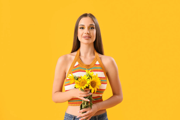 黄色の背景に美しいサンフラワーの花束を持つ若い女性 - 写真・画像