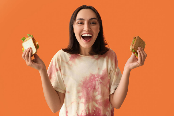Schöne junge Frau mit leckeren Sandwiches auf orangenem Hintergrund - Foto, Bild